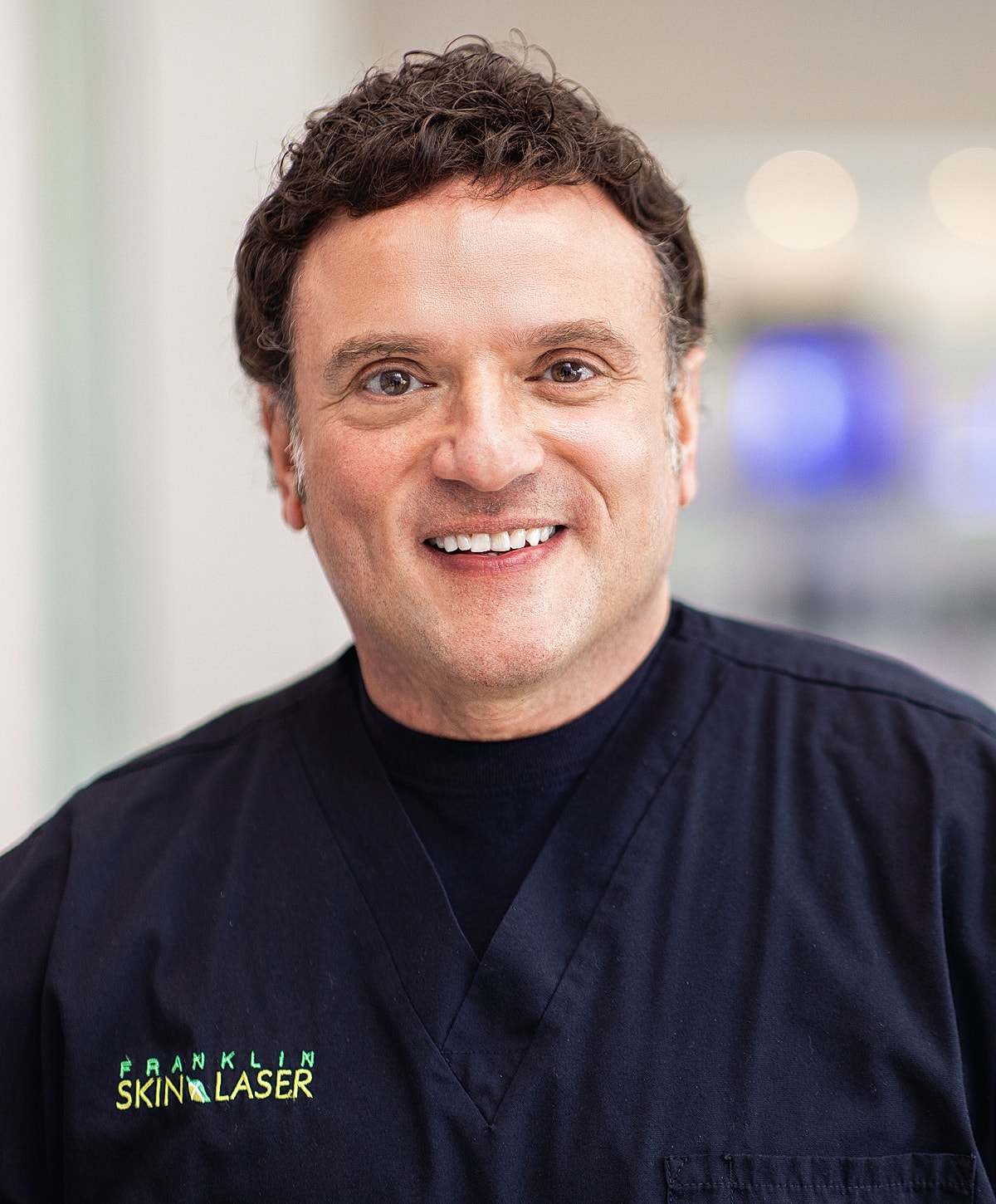 Smiling professional in medical scrubs with logo.