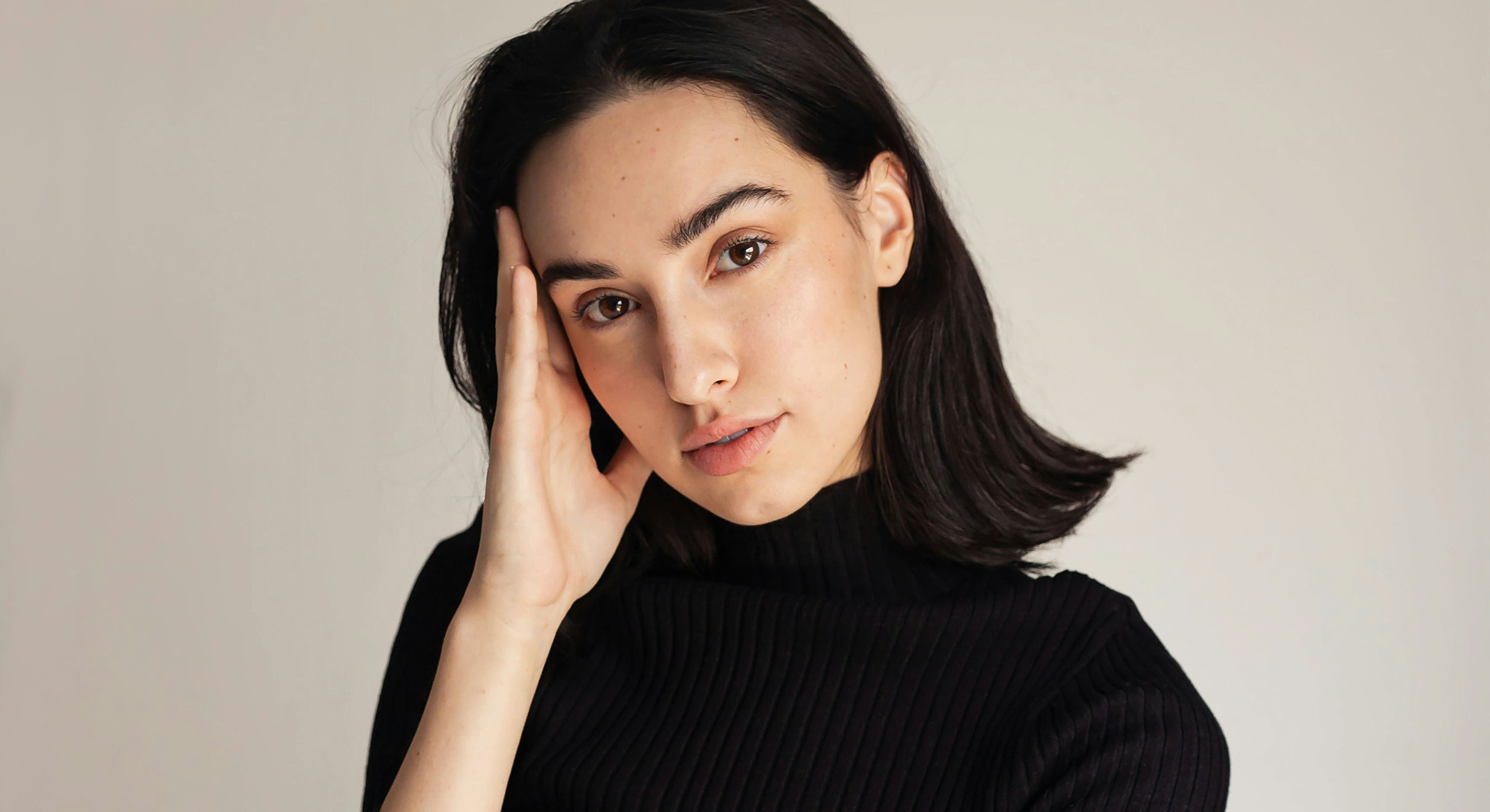 Woman with hand on face, neutral background.